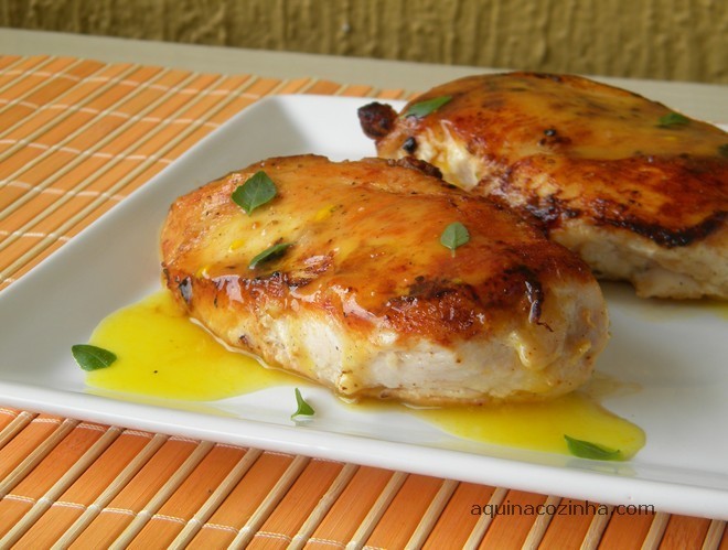 Filé de frango com molho de laranja em cima de um prato branco com ervas em cima