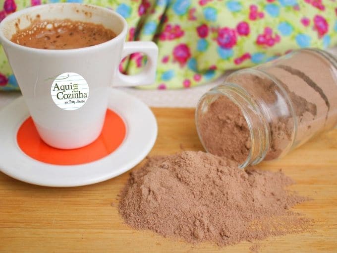 A imagem apresenta um recipiente com pó de cappuccino caído e uma xícara com cappuccino.